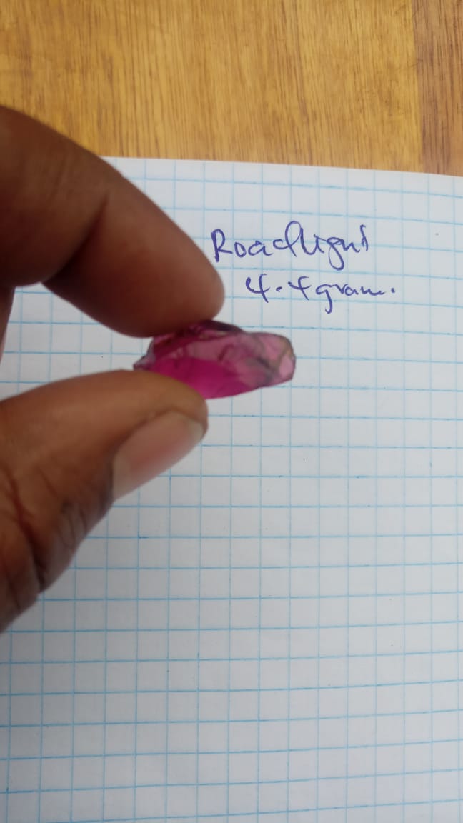 Rough coloured stone held above a written weight note